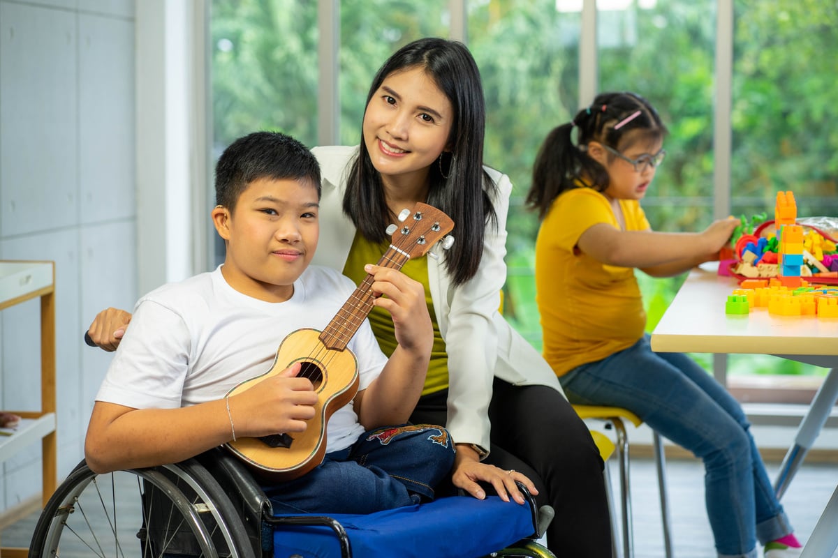 disability kid playing music with guitar on wheelchair with Autism child playing in special classroom